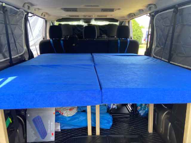 Van-Innenraum mit blauem Kombinationsbett, oben ausgezogen, unten verstaut unter blauer Matratze
