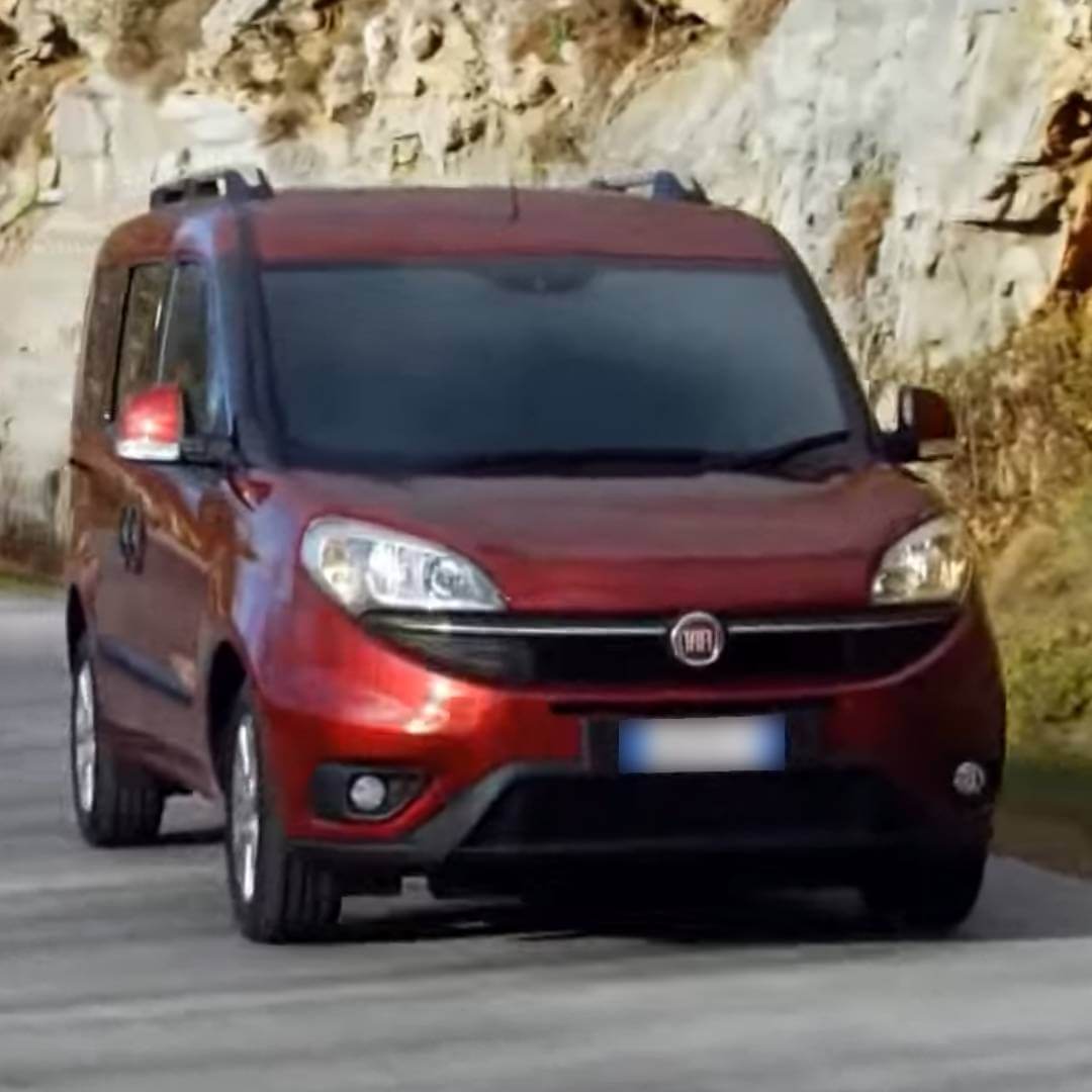 Fiat Doblo II Kleinbus in Rot, Frontansicht mit aktivierten Scheinwerfern an Bergstraße