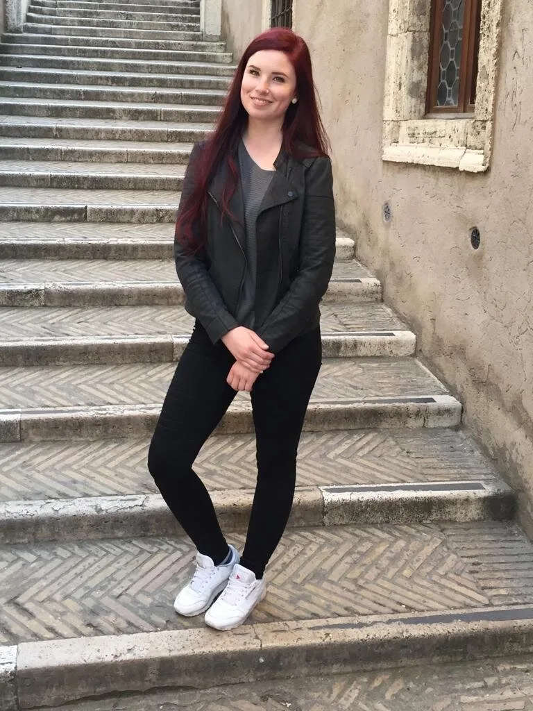 Lockere Frisuren – Videokurs für Hochsteckstyling von Laurie Ibsen 9 Junge Frau mit burgunderfarbenen Haaren auf historischen Steinstufen in schwarzer Jacke