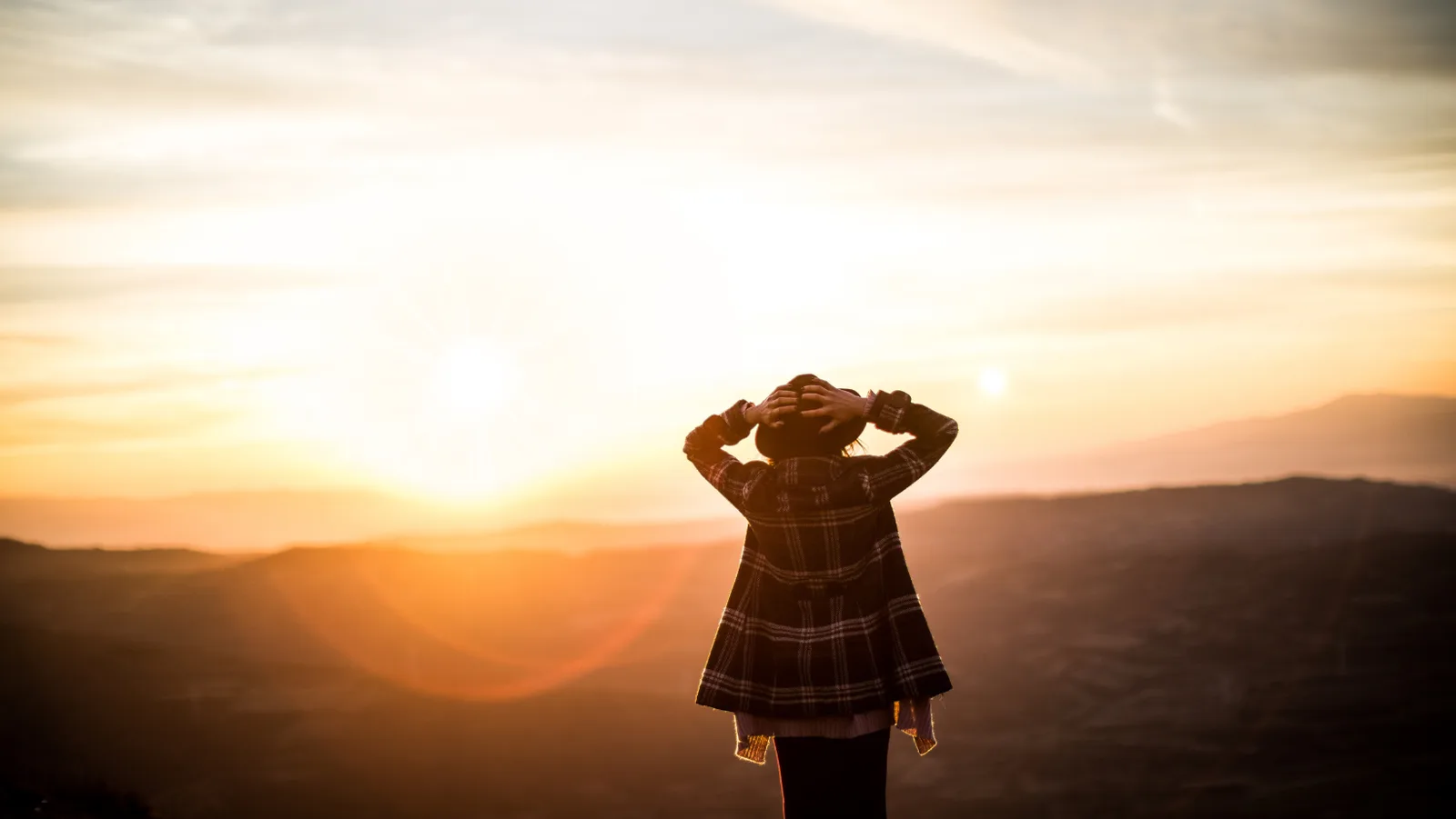 Frau in Karobluse bei Sonnenaufgang in Bergen, Hände am Kopf, Berglandschaft