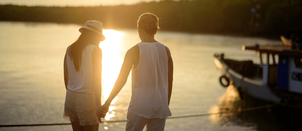 Paar hält sich an den Händen beim Sonnenuntergang am Wasser – Beziehungs- und Paartherapie Symbolbild
