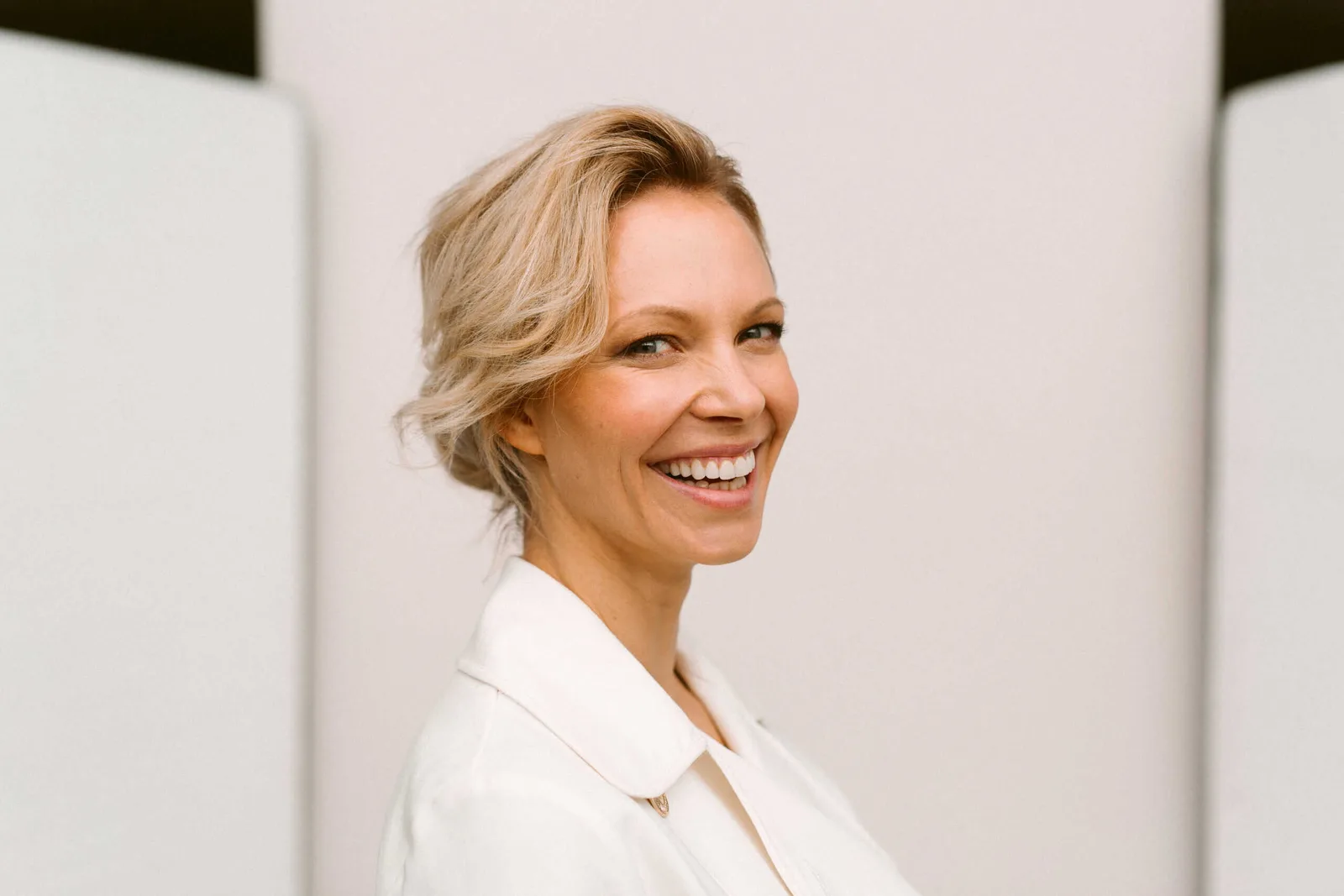 Birte Glang lächelt in weißem Blazer vor neutralem Hintergrund, MamaGlow Coaching Hero-Bild