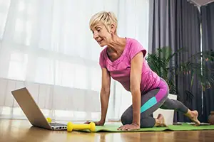 Frau trainiert vor Laptop zu Hause in pinker Sportkleidung
