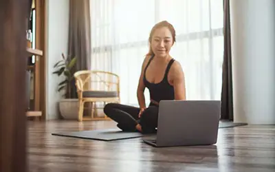 Frau in Sportkleidung sitzt vor Laptop und trainiert zu Hause