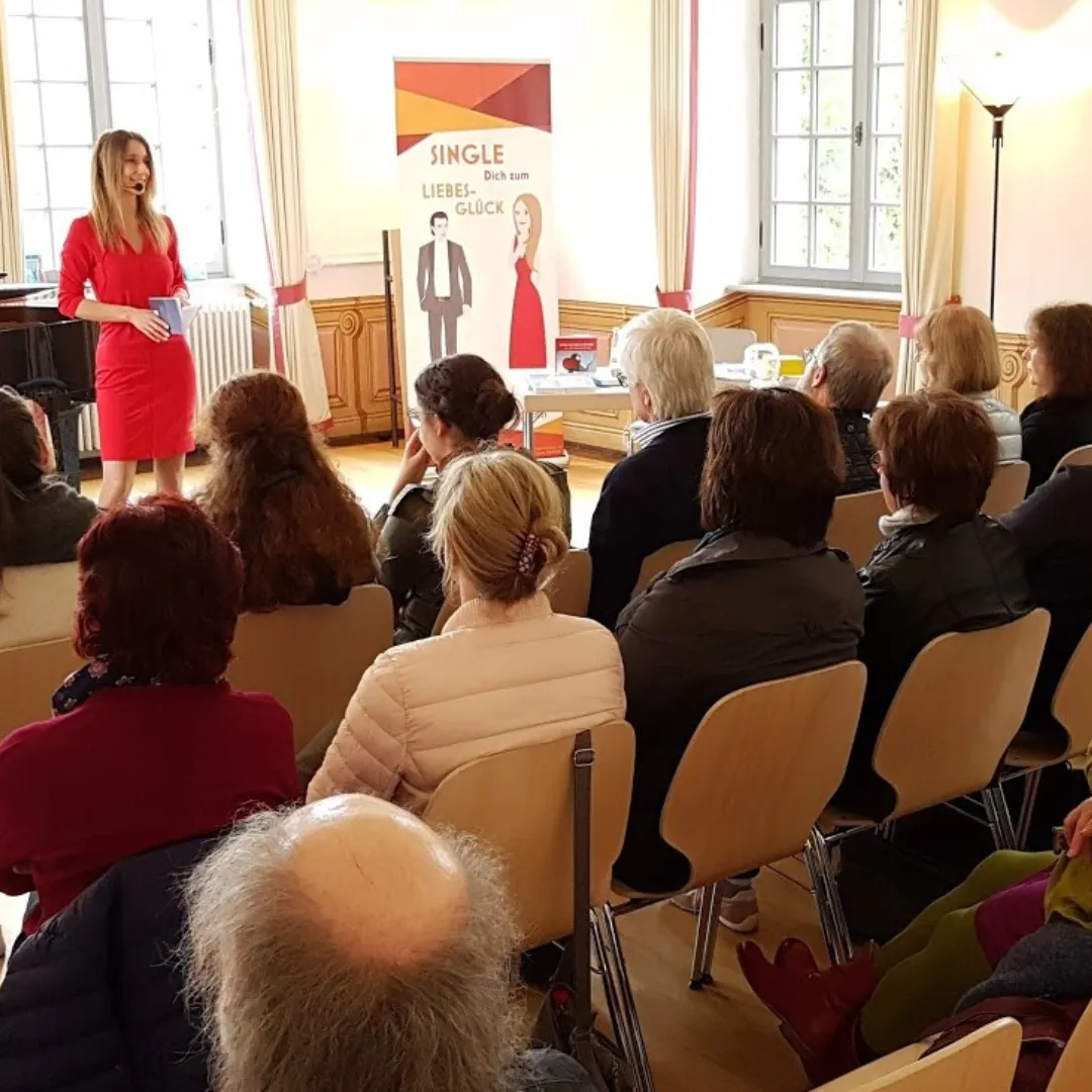 Präsentation von Die Frau in Rot in rotem Kleid vor Publikum mit Single-Liebe-Glück-Banner