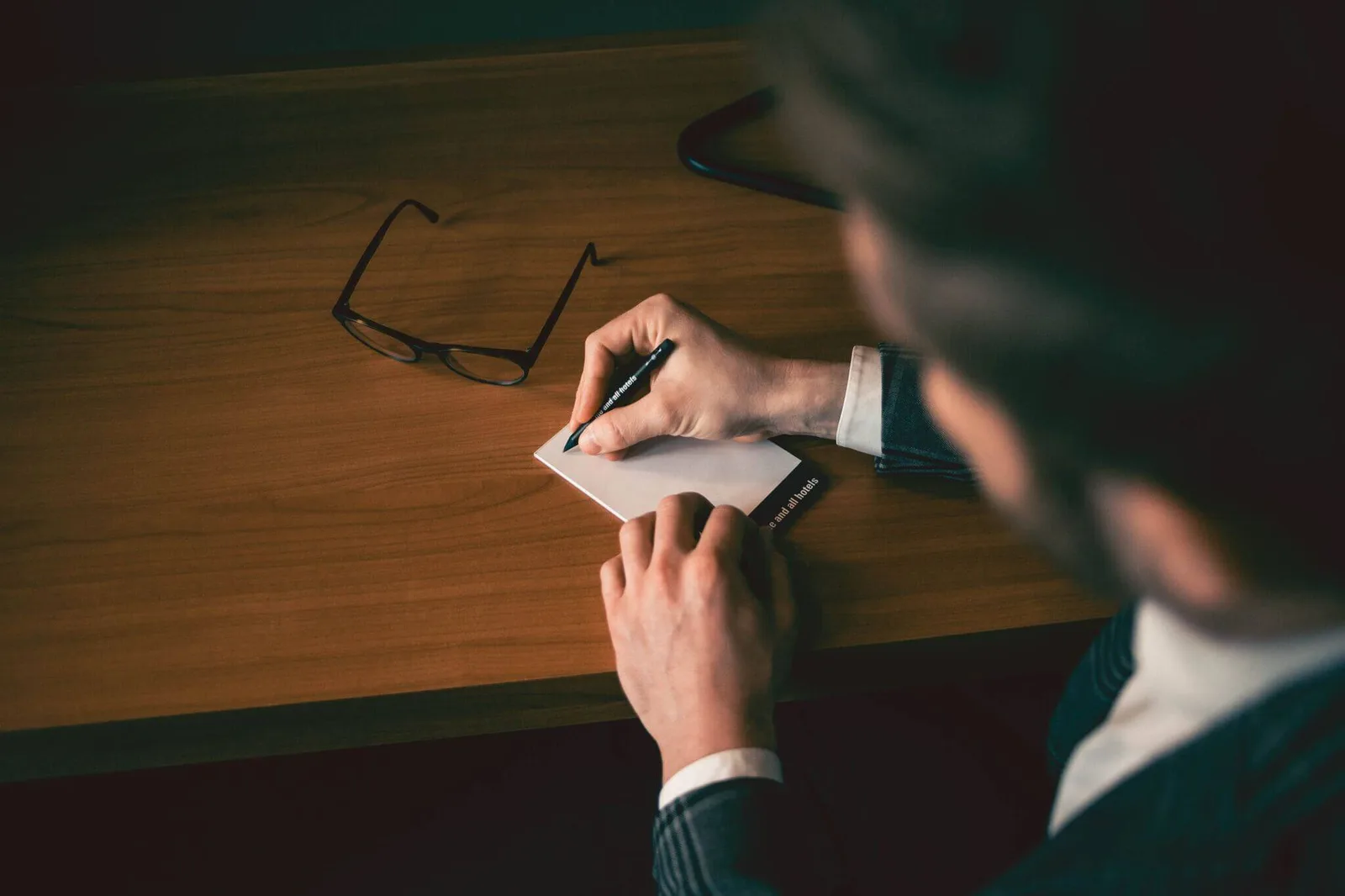 Marketing MasterClass – Videokurs zu Positionierung und Marke 4 Hände schreiben mit Marker auf kleinem Notizbuch, Brille und Holztisch sichtbar
