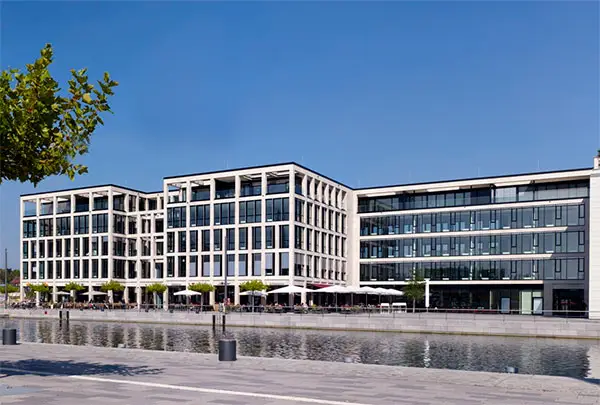 Moderne Geschäftsgebäude mit Glasfassaden an Wasserplatz unter blauem Himmel