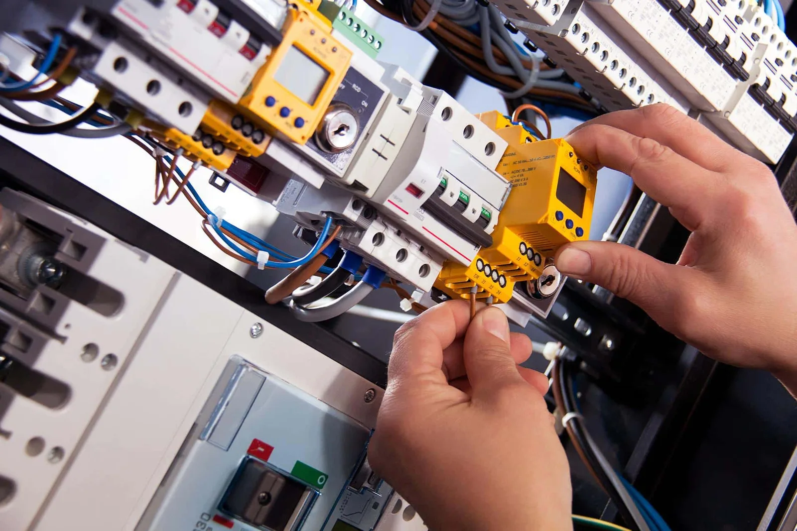 Elektrofachkraft arbeitet an Schaltschrank mit Messgeräten und farbigen Drähten