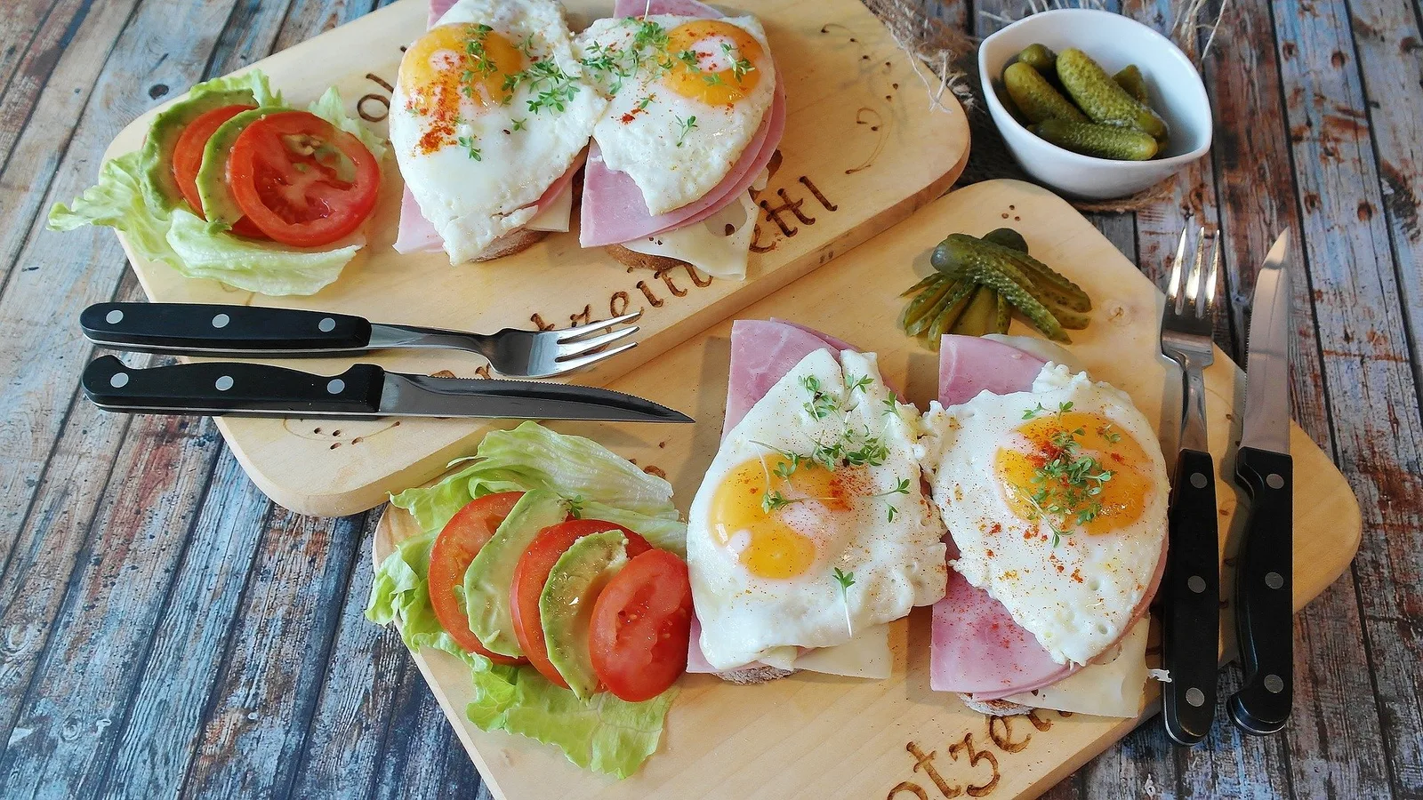 Belegte Brote mit Eiern, Schinken, Tomaten und Salat sowie eingelegte Gurken auf Holztablett