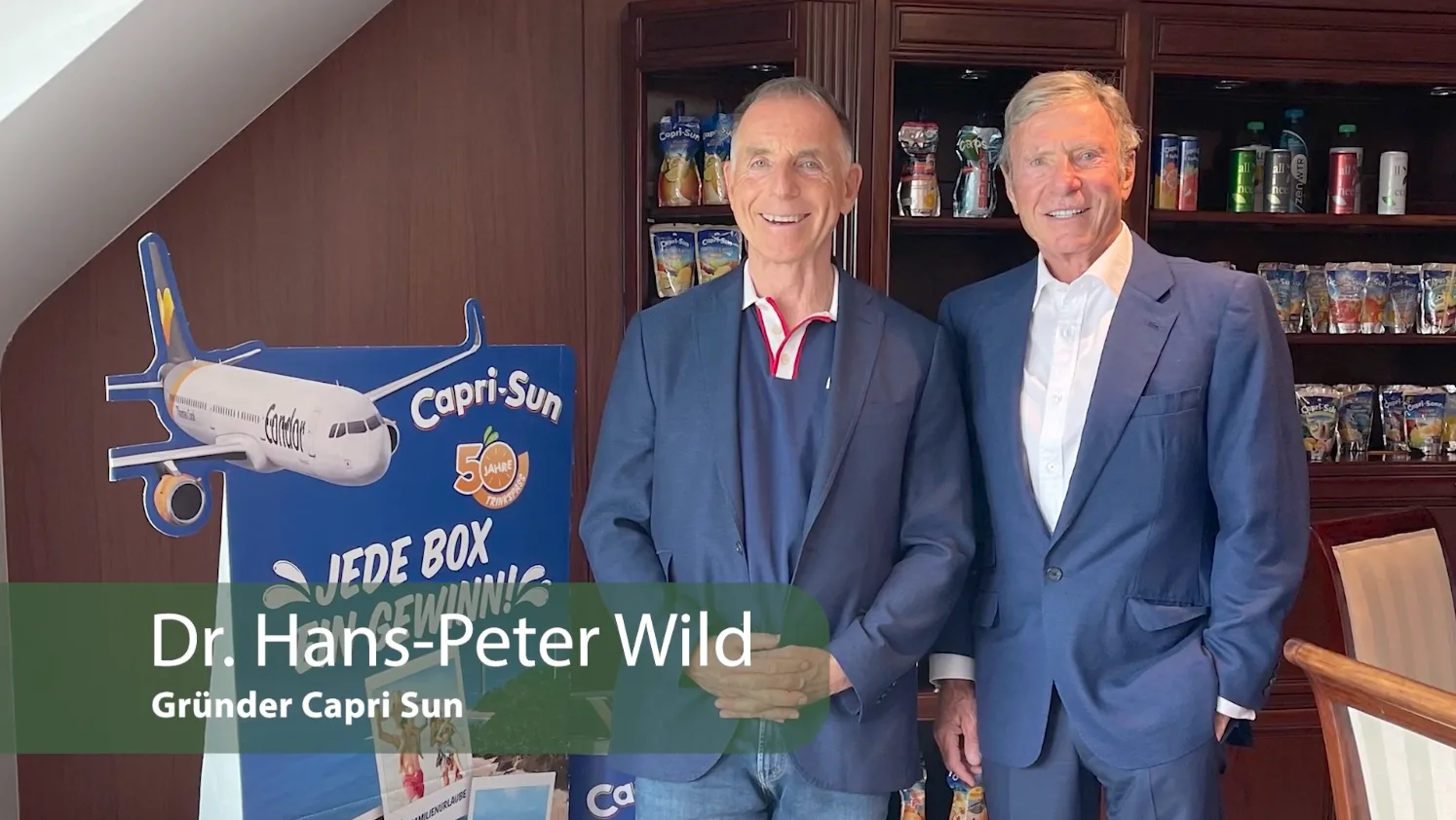 Master-Class Finanzielle Freiheit – Videokurs zum Vermögensaufbau 6 Dr. Hans-Peter Wild und weiterer Mann in Anzügen vor Capri-Sun Flugzeug-Display