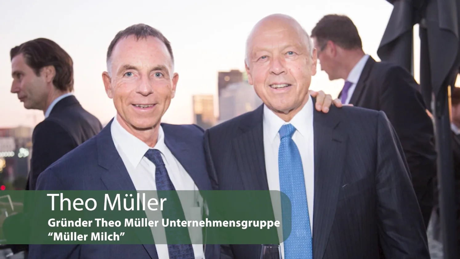 Master-Class Finanzielle Freiheit – Videokurs zum Vermögensaufbau 7 Theo Müller in Anzug mit Krawatte auf Business-Event mit Stadtkulisse