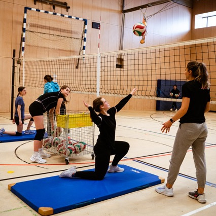 Jugendliche beim Volleyballtraining in einer Halle mit Trainerin auf blauer Matte