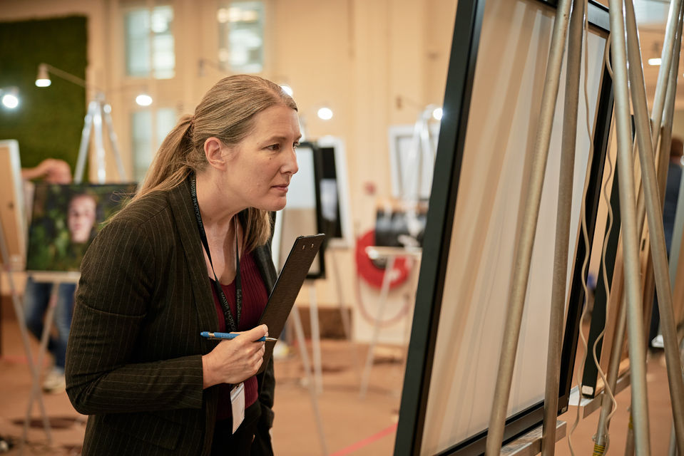 Frau in schwarzem Blazer und Weininrot betrachtet mehrere Fotografien in Galerie-Ausstellung