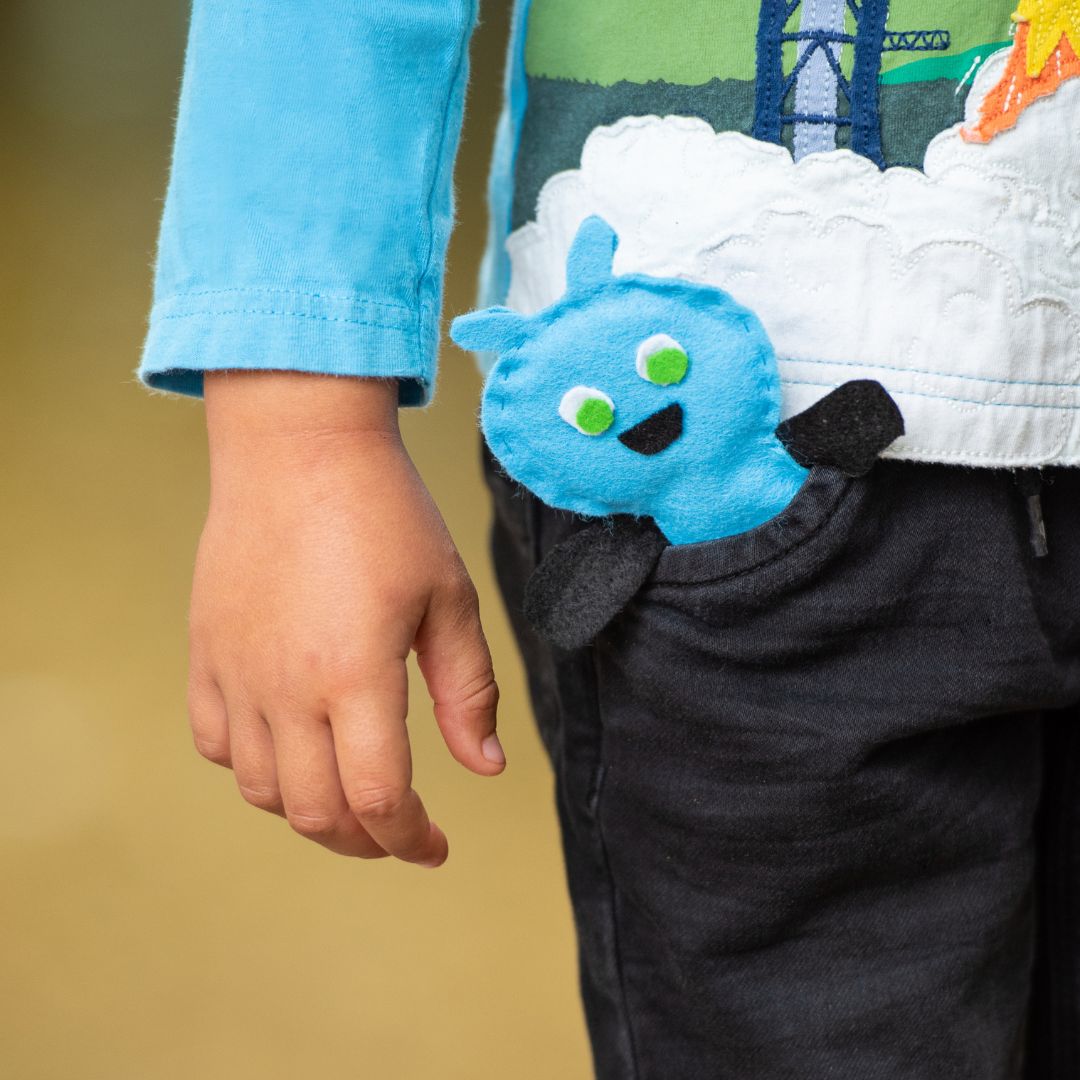 Glühwürmchen-Coaching – Kinderhand hält blauen Stoff-Charakter mit grünen Augen und lächelndem Mund