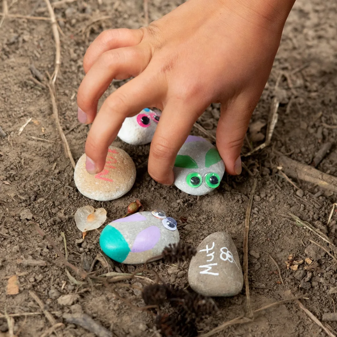 Mutsteine - Coaching für Kinder – Kinderhand mit bemalten Steinen, die mit Gesichtern und Mut-Symbolen verziert sind