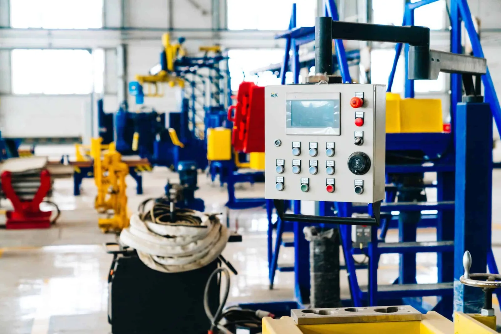 Mechatroniker AP2 – IHK-Prüfungsvorbereitungskurs von Christoph Höller 10 Industrie-Werkstatt mit Maschinen, fokussiert auf moderne Steuerungsanlage mit Display in Vordergrund, gelbe und blaue Geräte