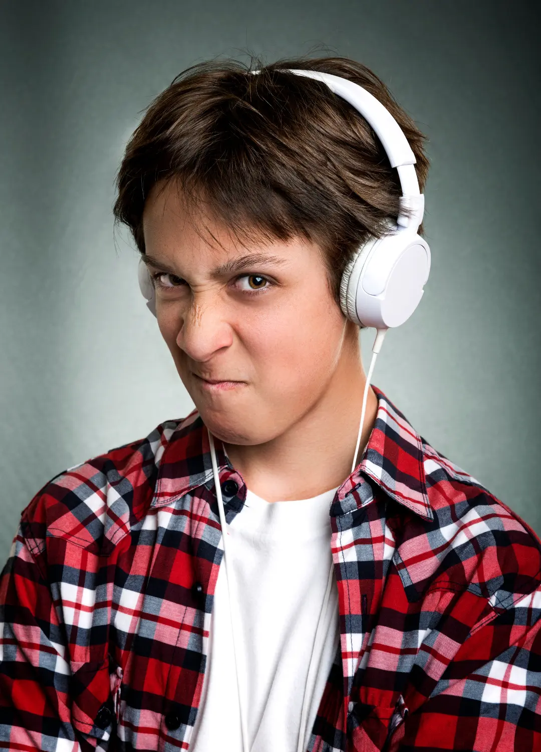 Jugendlicher mit weißen Kopfhörern und kariertem Hemd, skeptischer Blick