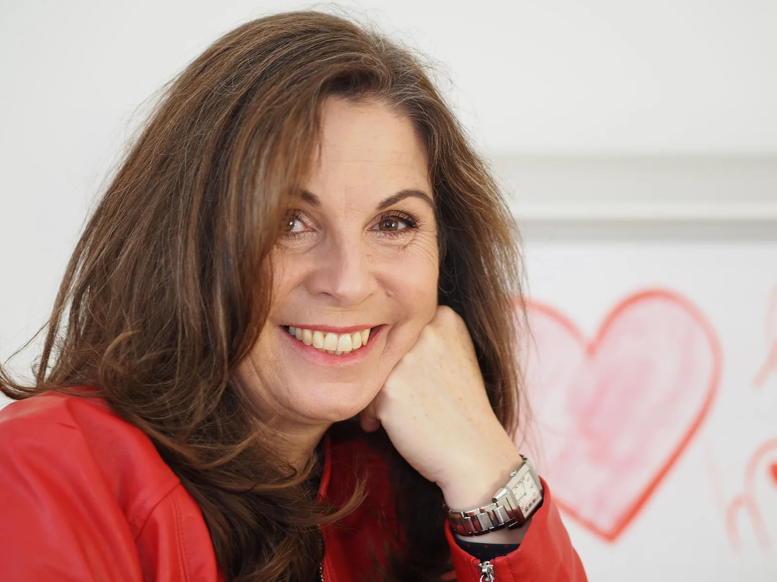 Ines Berger, Autorin, Porträt in rotem Shirt lächelnd mit rosa Herz-Dekoration