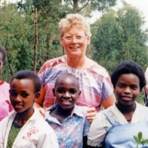 Ältere blonde Frau mit Bluse umgeben von drei jungen afrikanischen Frauen im Freien vor grünem Hintergrund
