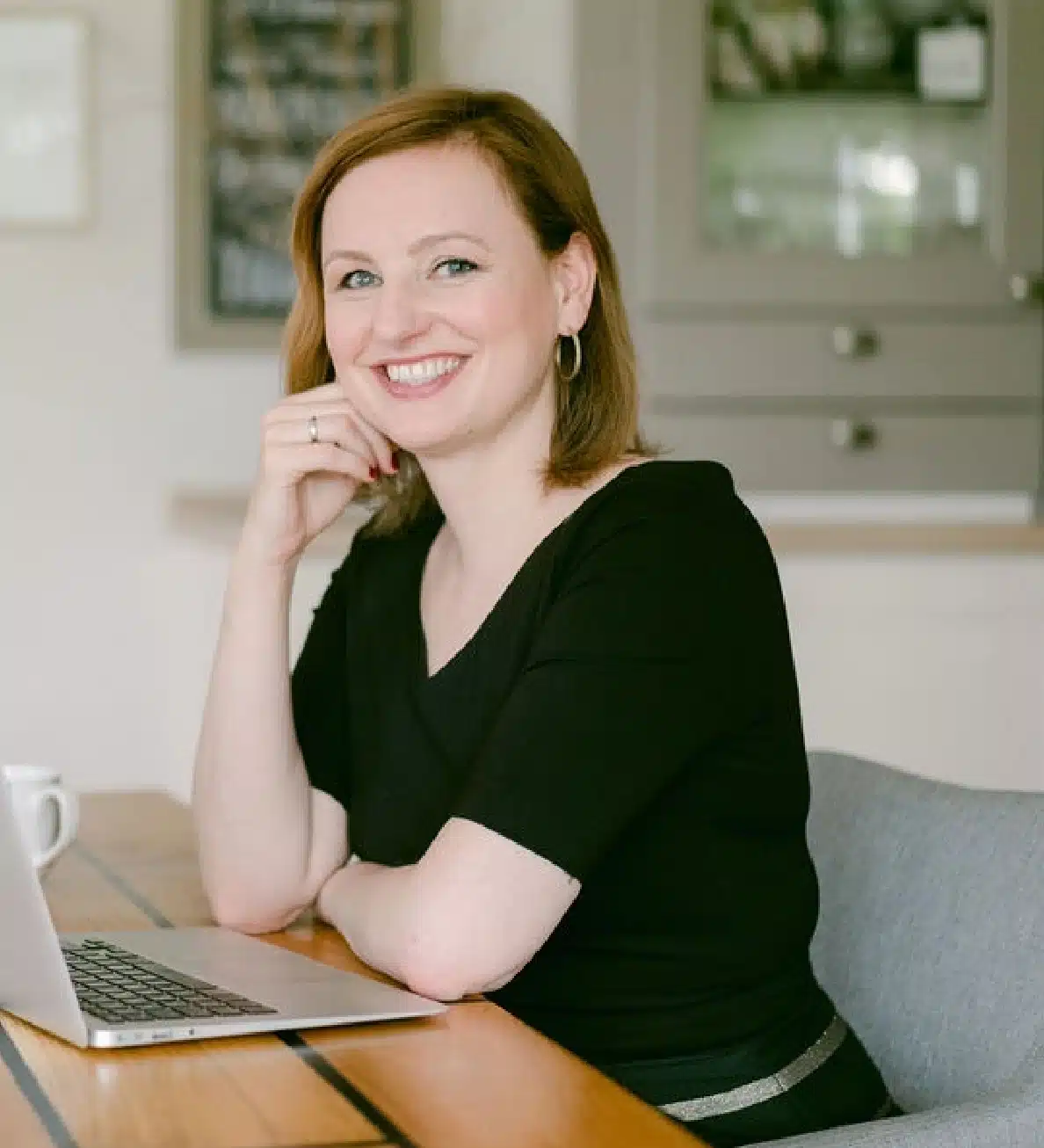 Marike Frick, rotbraunes Haar, schwarzes Oberteil, Porträt am Schreibtisch mit Laptop