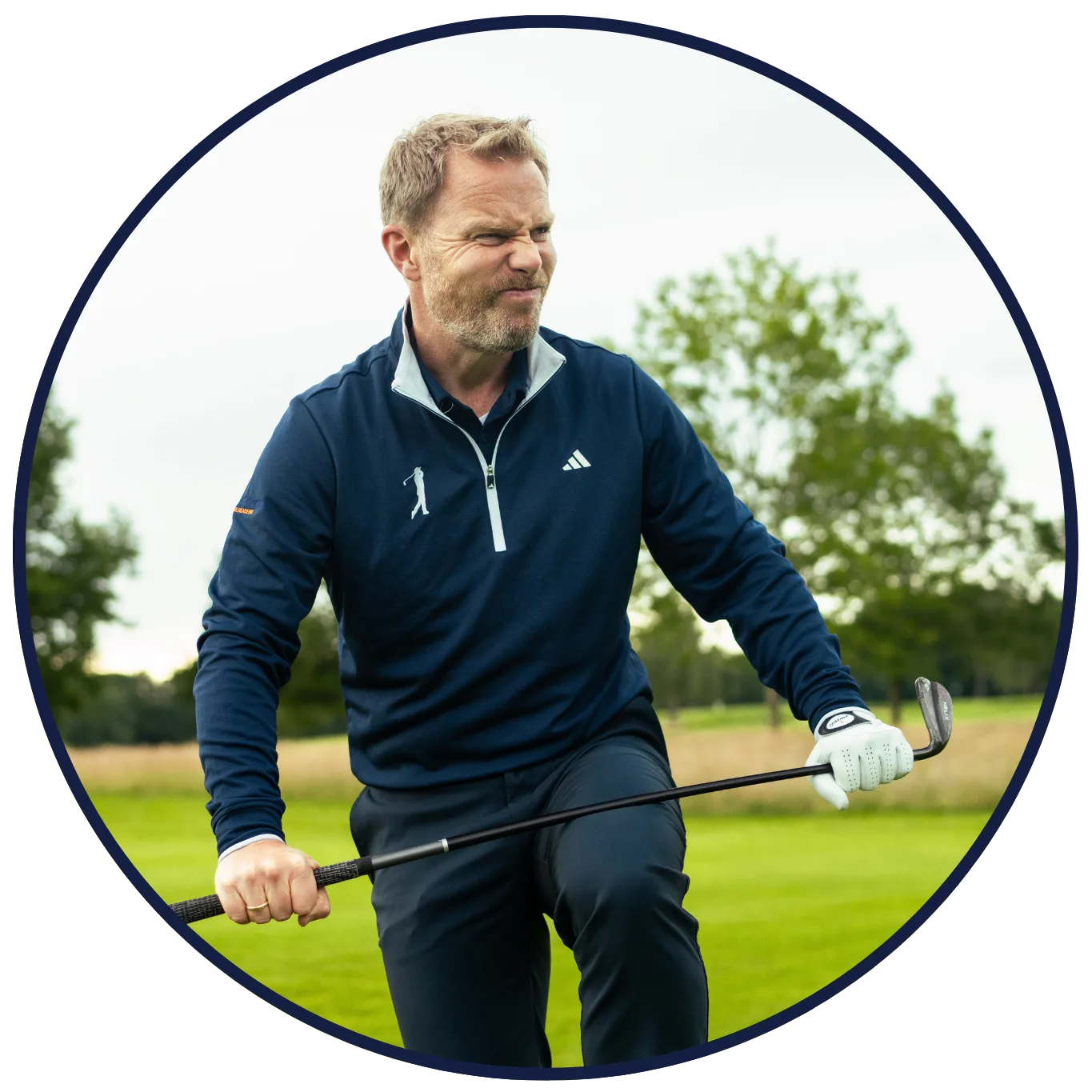 Porträt Fabian Bünker auf Golfplatz mit Schläger, dunkelblauer Adidas-Pullover mit Golfer-Logo