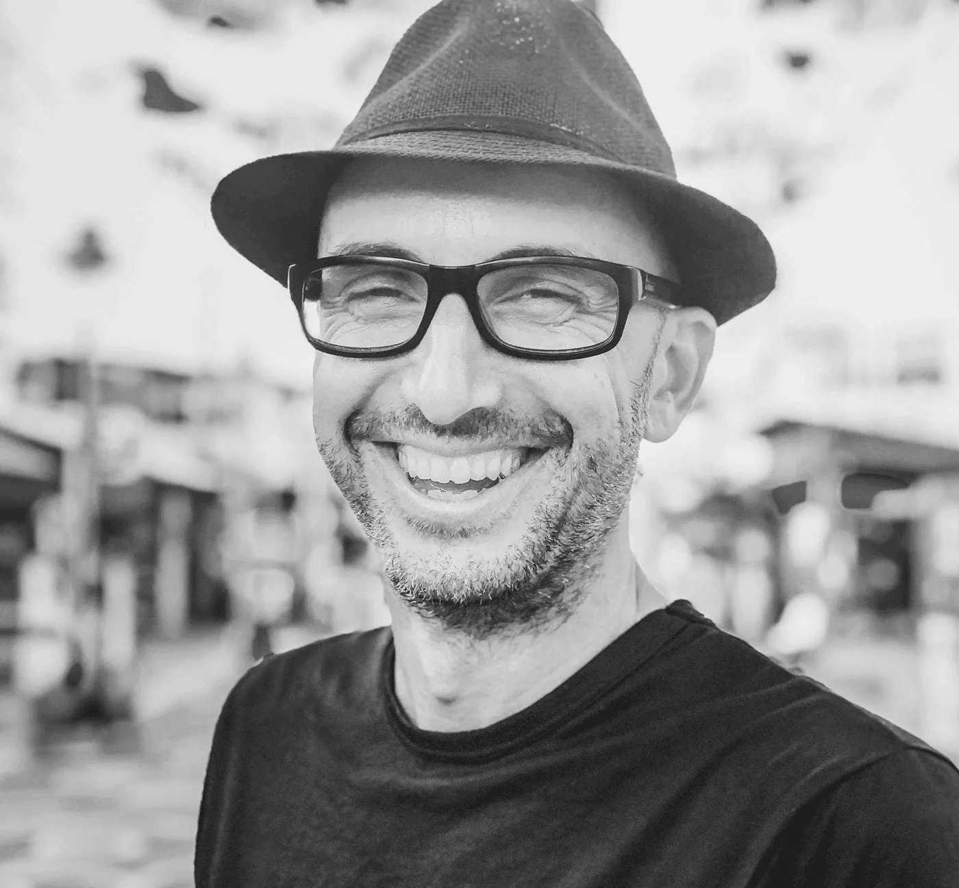 Marco Lachmann-Anke trägt Hut und Brille, schwarzweiß Porträt, lächelnd