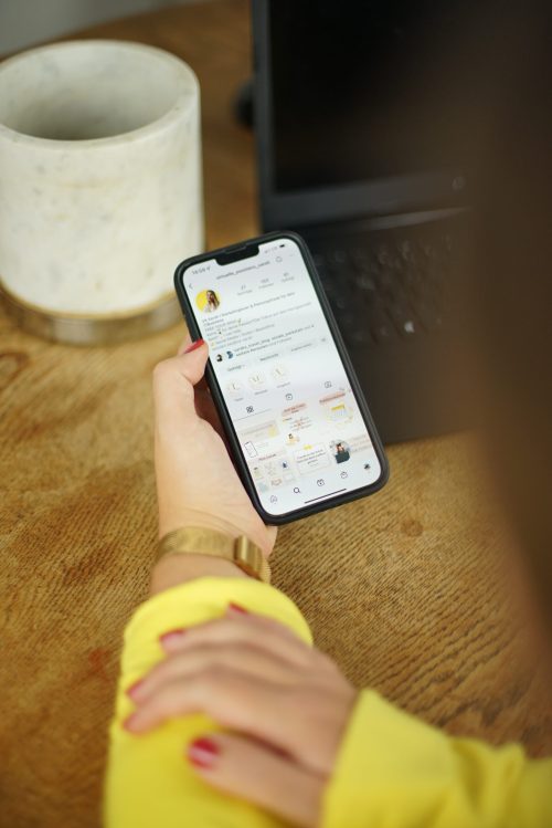 Meta Werbeanzeigen Teil 2 – Live-Workshop zu Facebook-Ads 5 Hand mit gelbem Armband hält Smartphone mit Instagram-Feed, Kaffeetasse im Hintergrund