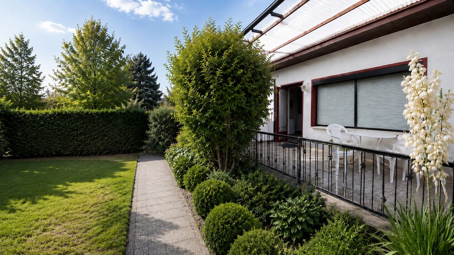 Gartenhaus mit moderner Terrasse, schwarzem Geländer, grünem Rasen und gepflegtem Gartenweg