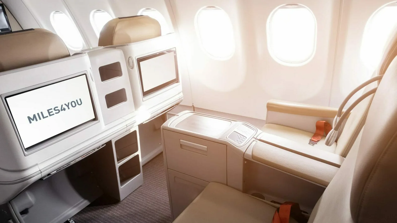 Business-Class-Kabine eines Flugzeugs mit beige-braunen Sitzen, Fenster mit Tageslicht, Bildschirm zeigt Miles4You-Logo