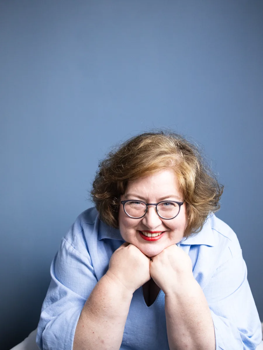 Sandra Dirks lächelt, die Hände unterm Kinn, vor blauem Hintergrund