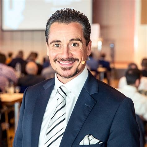 Businessman mit dunklem Anzug und Krawatte lächelnd vor unscharfem Konferenz-Hintergrund