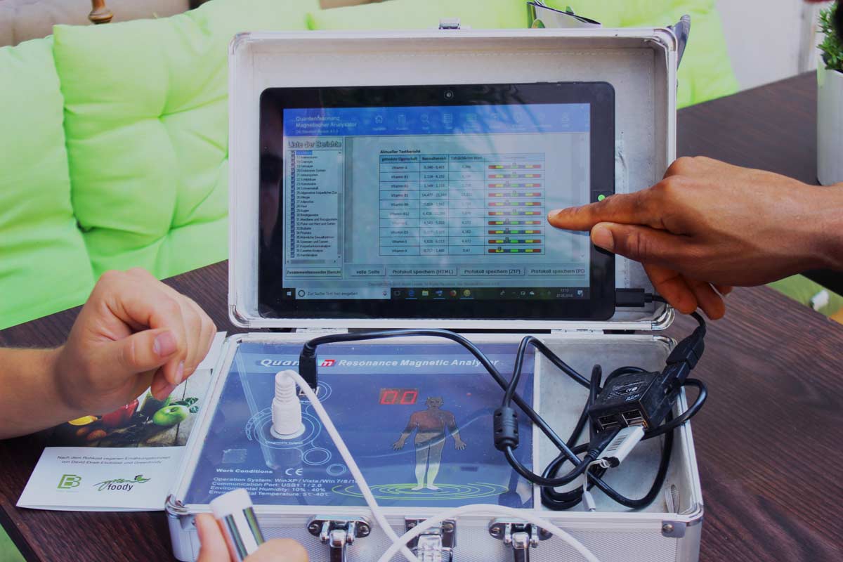 Bioscan-Gerät auf Laptop mit Analysedaten, Hände zeigen auf Bildschirm mit Messwerten