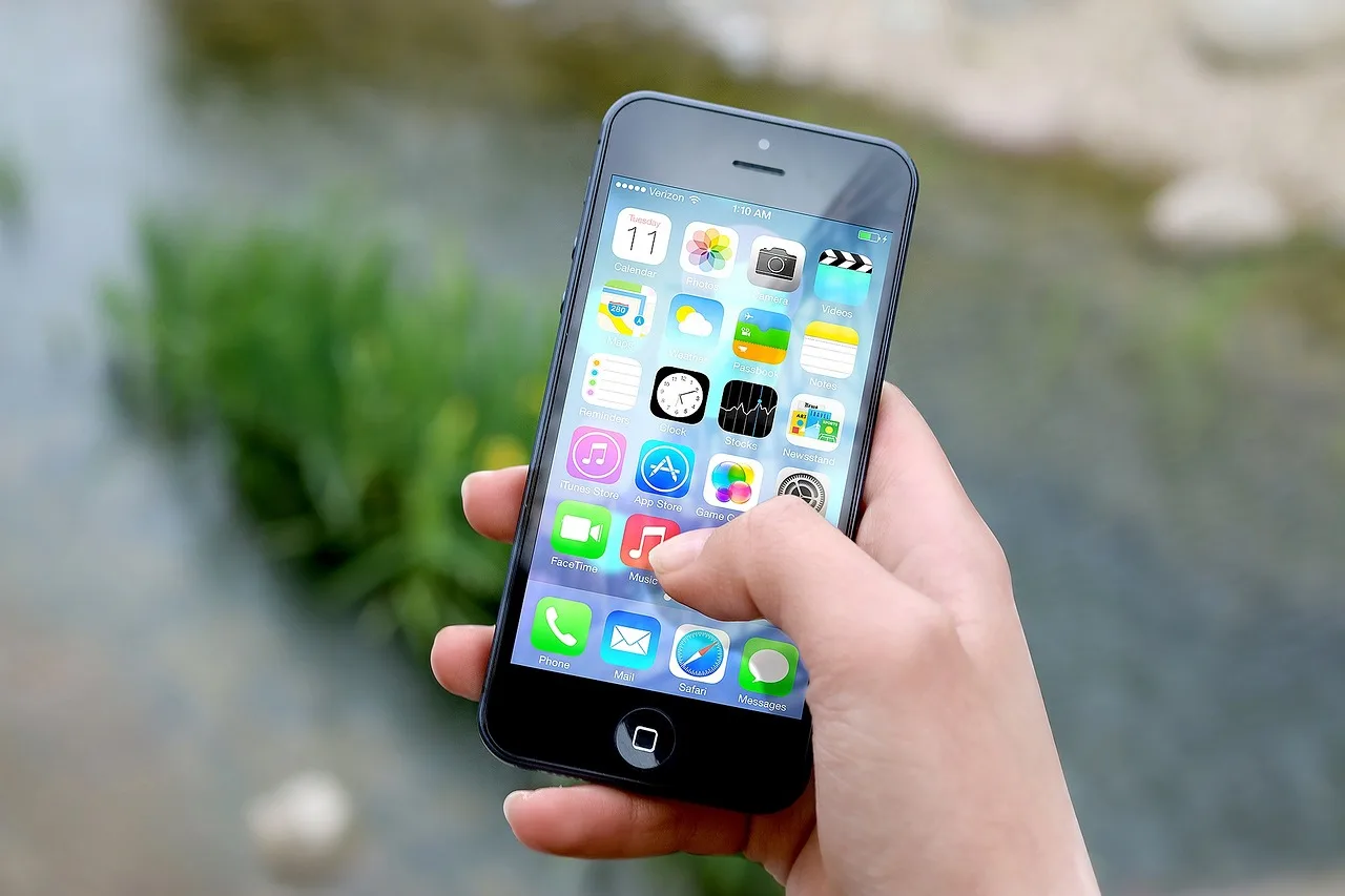 iPhone mit App-Icons auf dem Startbildschirm, in einer Hand gehalten vor unscharfem grünem Hintergrund