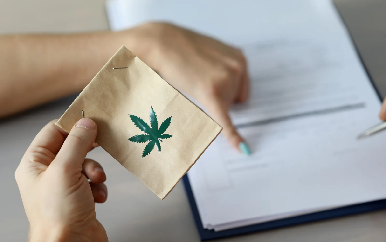 Hand hält Papiertüte mit grünem Cannabis-Blatt-Symbol über aufgeschlagenem Buch