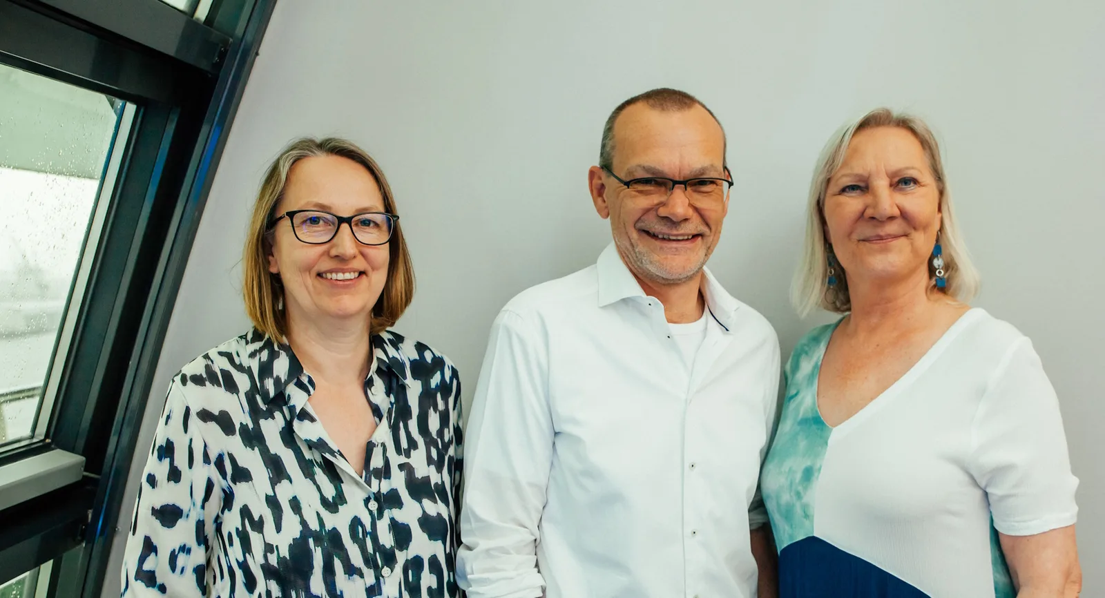 Modernes Projektmanagement – Nachschlagewerk zu Scrum und Kanban 4 Drei Personen Team Porträt vor grauer Wand, zwei Frauen und ein Mann lächelnd