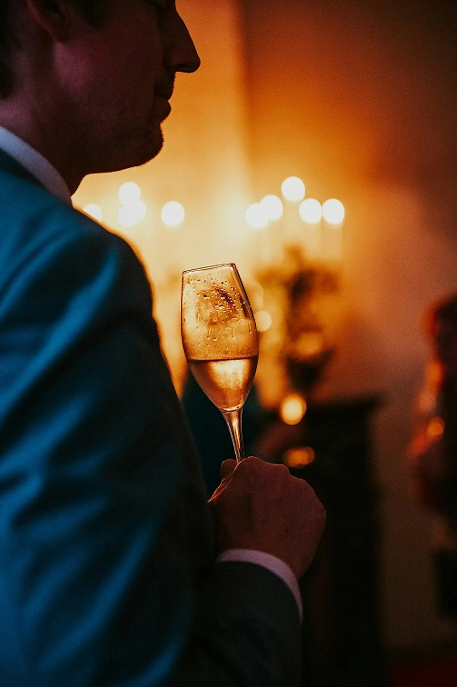 MONEY³ Mentoring – Coaching fürs Geld-Mindset von Daniel Weinstock 1 Mann mit Champagnerglas vor warmem, unscharfem Lichthintergrund