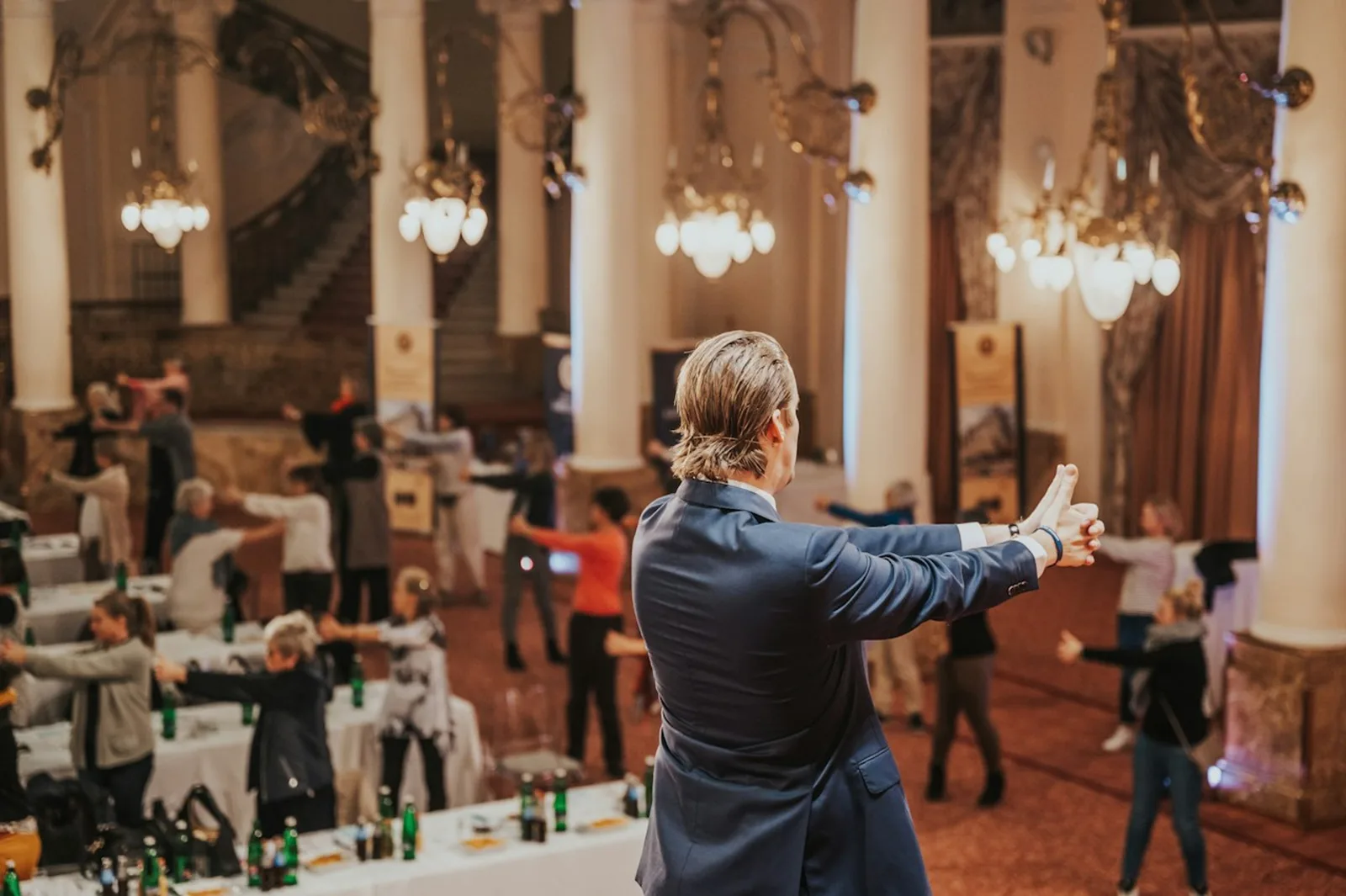 Redner mit ausgebreiteten Armen vor Publikum in eleganter Ballsaal