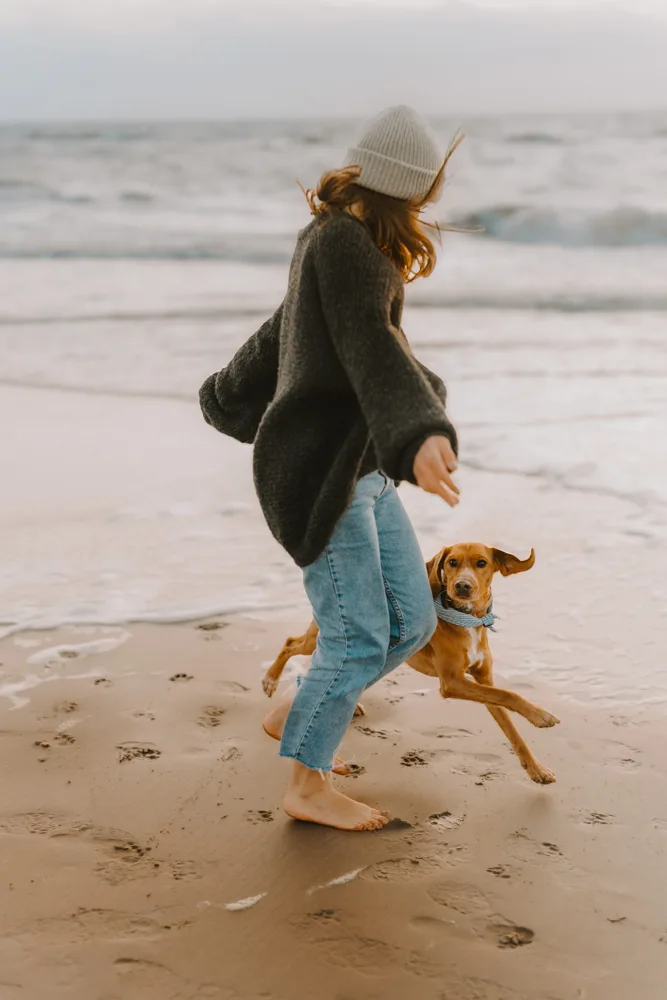 Frau springt mit braunem Hund am Strand, Motion Blur ohne Effekt