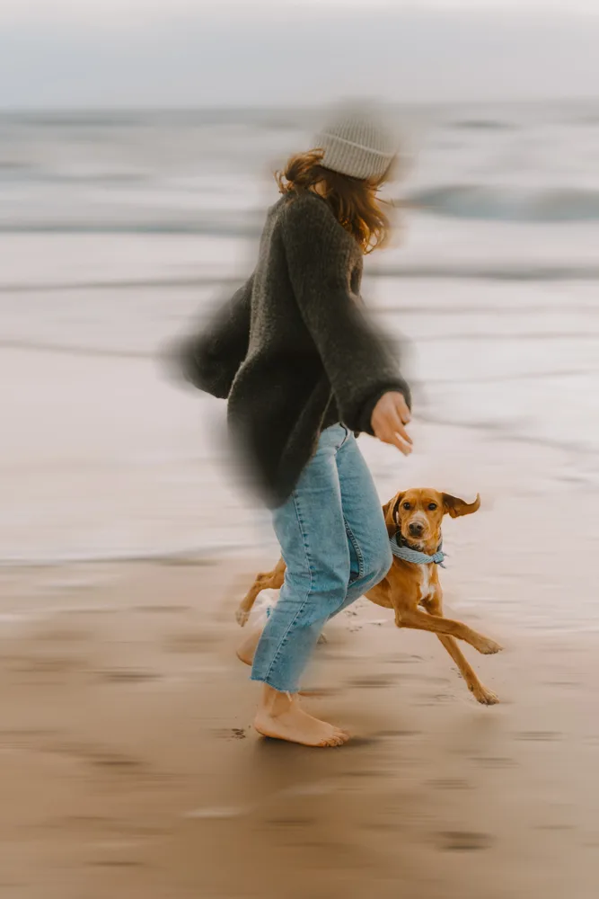 Frau springt mit braunem Hund am Strand mit Motion Blur Effekt