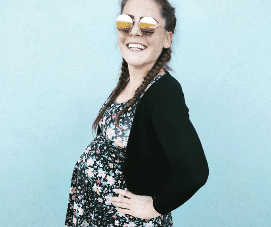 Lächelnde Frau mit Zöpfen und Sonnenbrille in Blumenmuster-Outfit