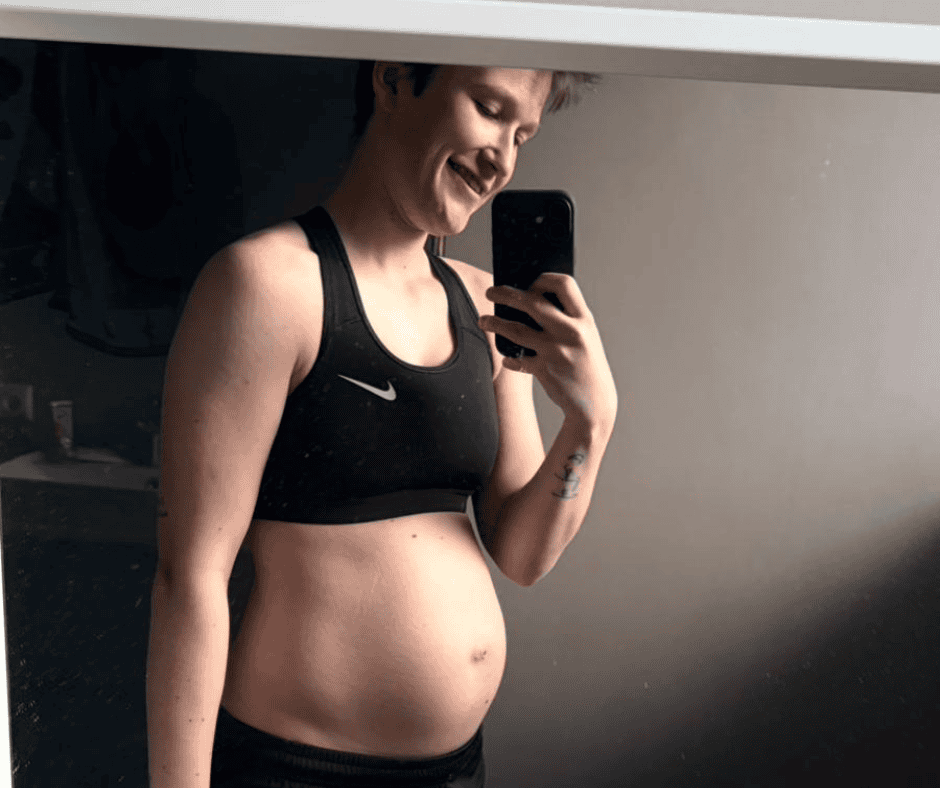 Schwangere Frau in schwarzem Sportoutfit macht Selfie mit Lächeln