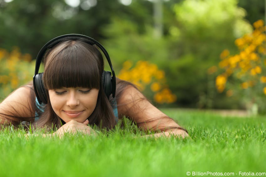 MP3-Lizenz Trancemusik – Audiopaket für Hypnosearbeit 7 Kind mit Kopfhörern liegt auf grünem Rasen, hört Musik und genießt Natur