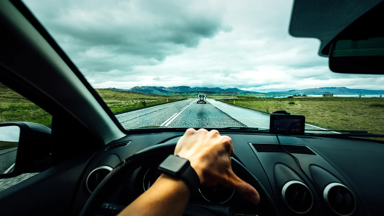 Blick aus Fahrzeug auf Autobahn mit grüner Landschaft und Bergen im Hintergrund