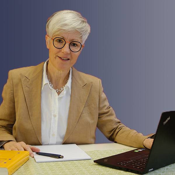 Sabine Keinath sitzt am Schreibtisch mit Laptop, Notizblock und Stift für kostenfreies Erstgespräch