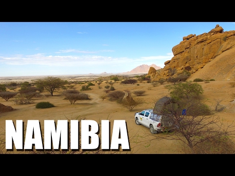 Luftaufnahme eines weißen 4x4-Fahrzeugs in Namibias Wüstenlandschaft mit Felsformationen