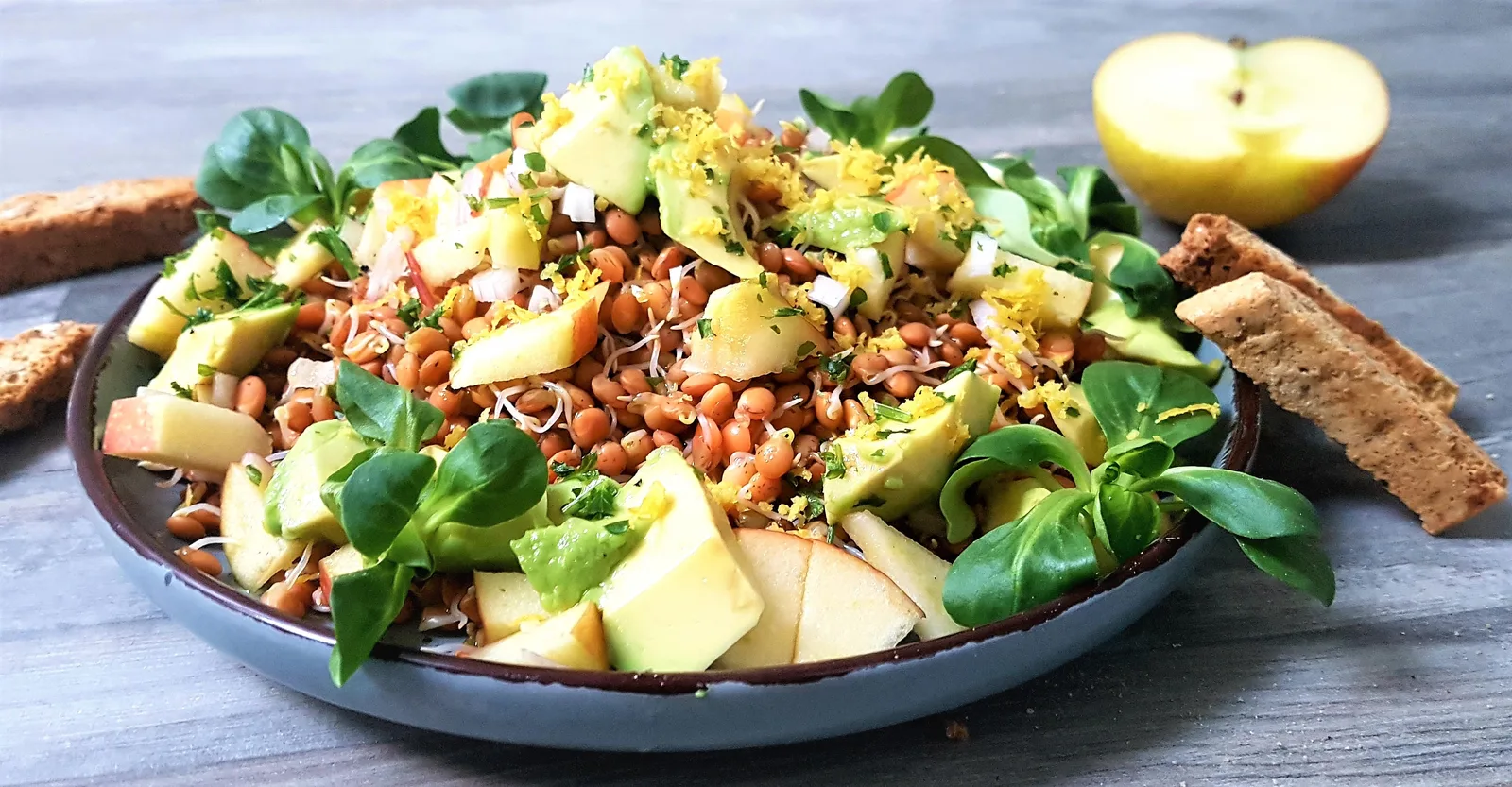 Linsensprosse Salat mit Avocado, Apfel und Vollkornbrot auf dunklem Teller, Ernährungsberatung Rezept