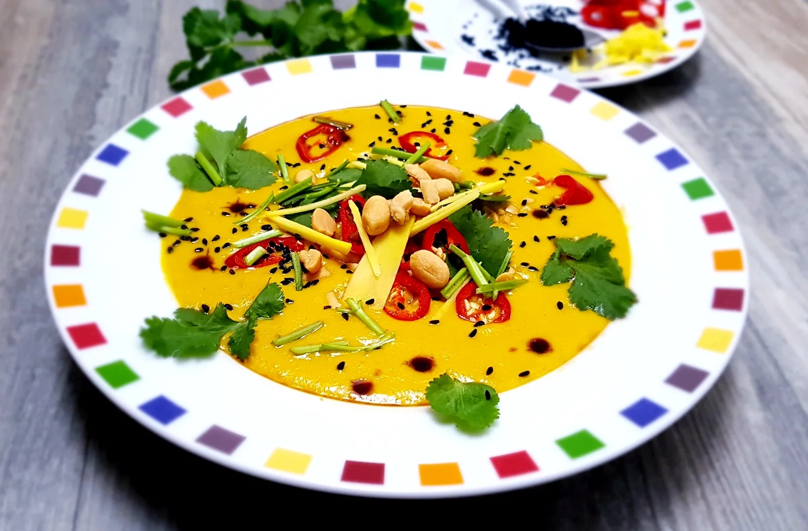 Süßkartoffelsuppe gelb mit Erdnüssen, Koriander und Chili auf buntem Teller, asiatisches Rezept