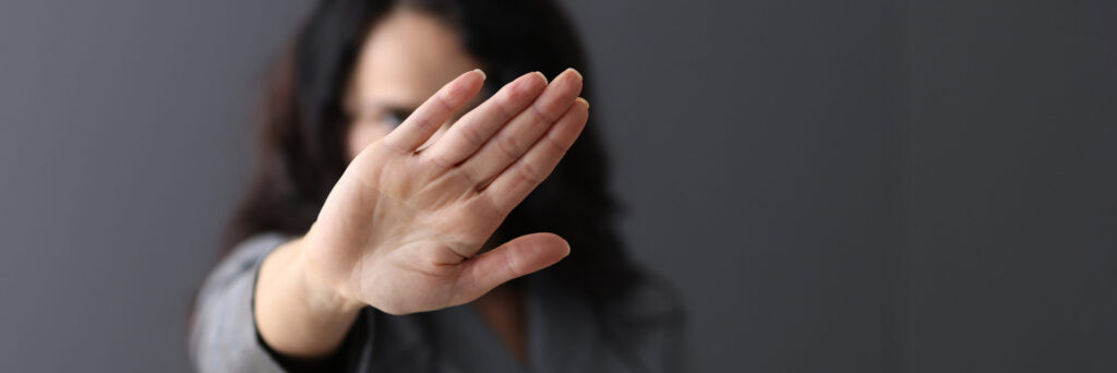 Frau macht mit ausgestreckter Hand Stop-Geste, verschwommener Hintergrund, klare Ablehnung