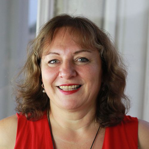 Meike Hohenwarter, Frau mit braunem welligem Haar in rotem Oberteil, lächelnd
