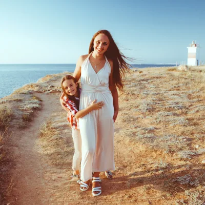 Frau mit Kind am Strand in weißem Kleid, Leuchtturm im Hintergrund